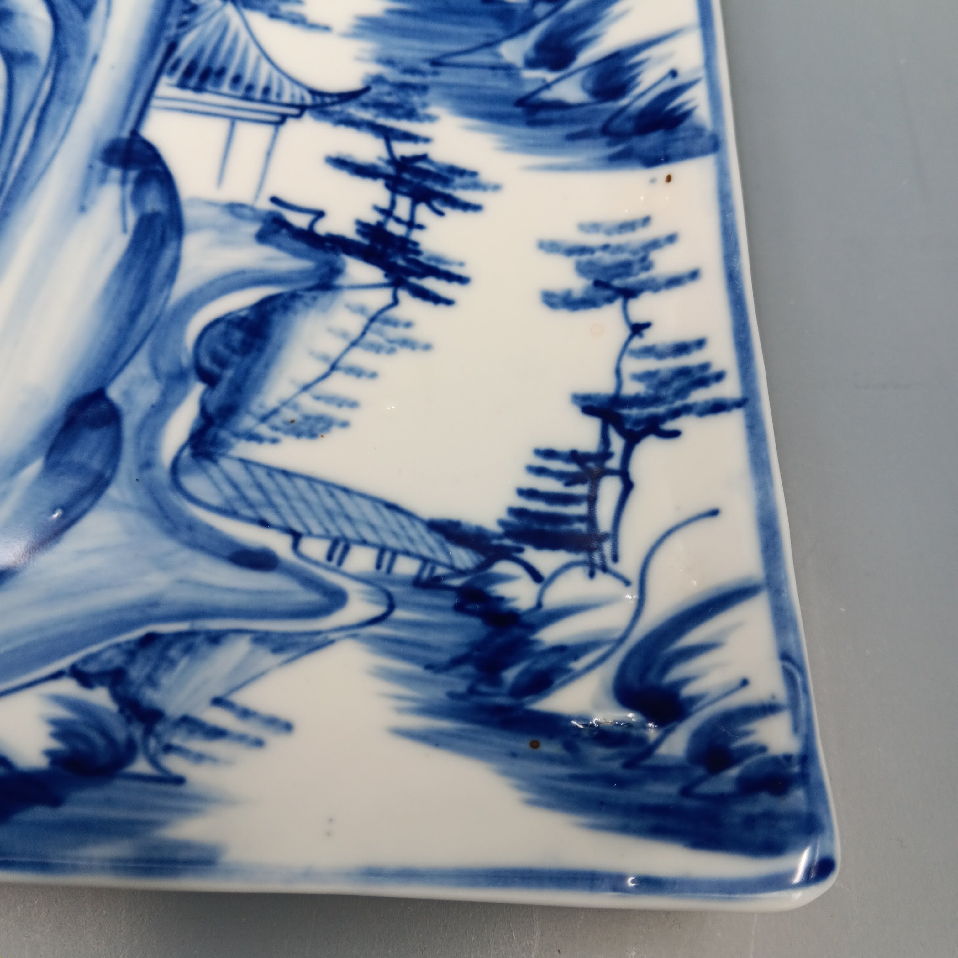 Antique Chinese blue and white porcelain plate with hand-painted landscape scene featuring mountains, trees, and a pavilion in cobalt blue on a rectangular ceramic dish.