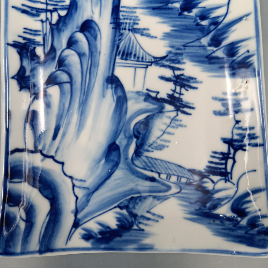 Antique Chinese blue and white porcelain dish with hand-painted landscape scene featuring mountains, trees, and a pavilion in cobalt blue on a rectangular ceramic dish."