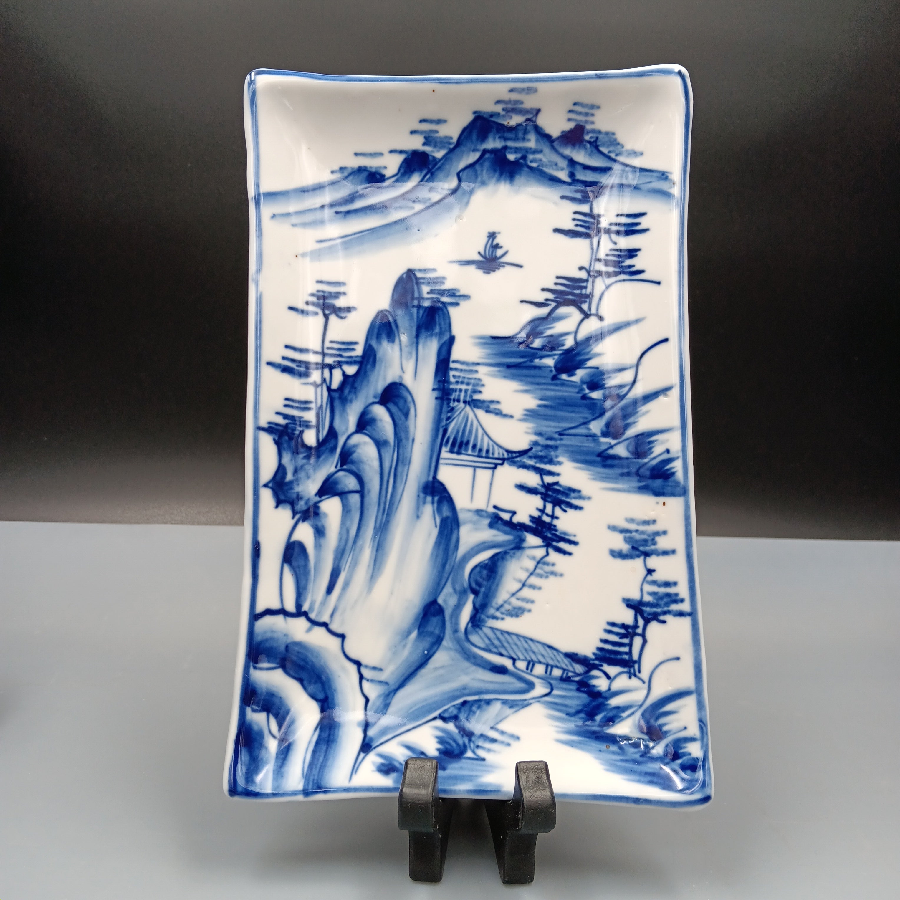 Antique Chinese blue and white porcelain plate with hand-painted landscape scene featuring mountains, trees, and a pavilion in cobalt blue on a rectangular ceramic dish.