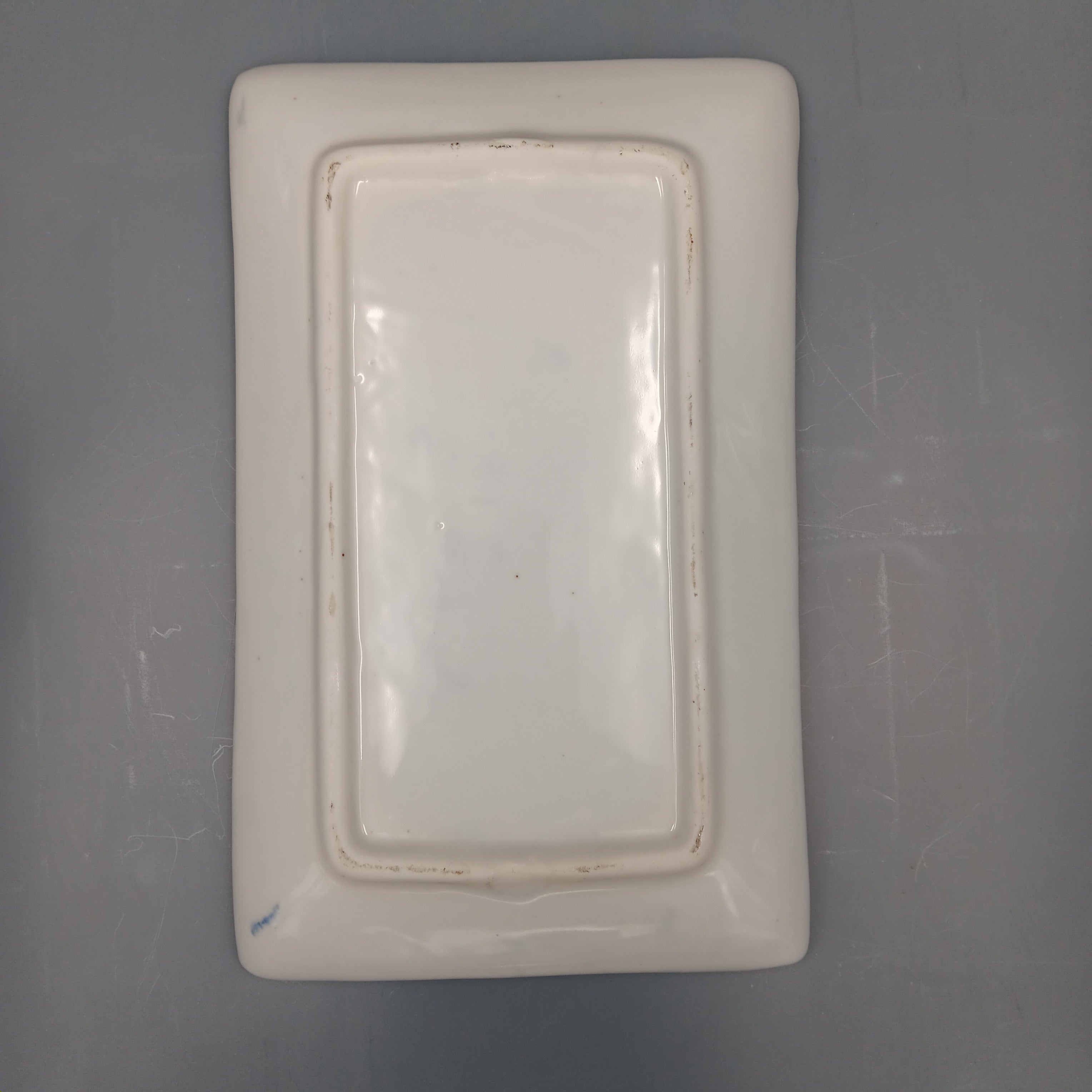 Underside of a rectangular white porcelain plate showing raised foot rim and subtle kiln marks, indicative of late Qing to early Republic period craftsmanship.