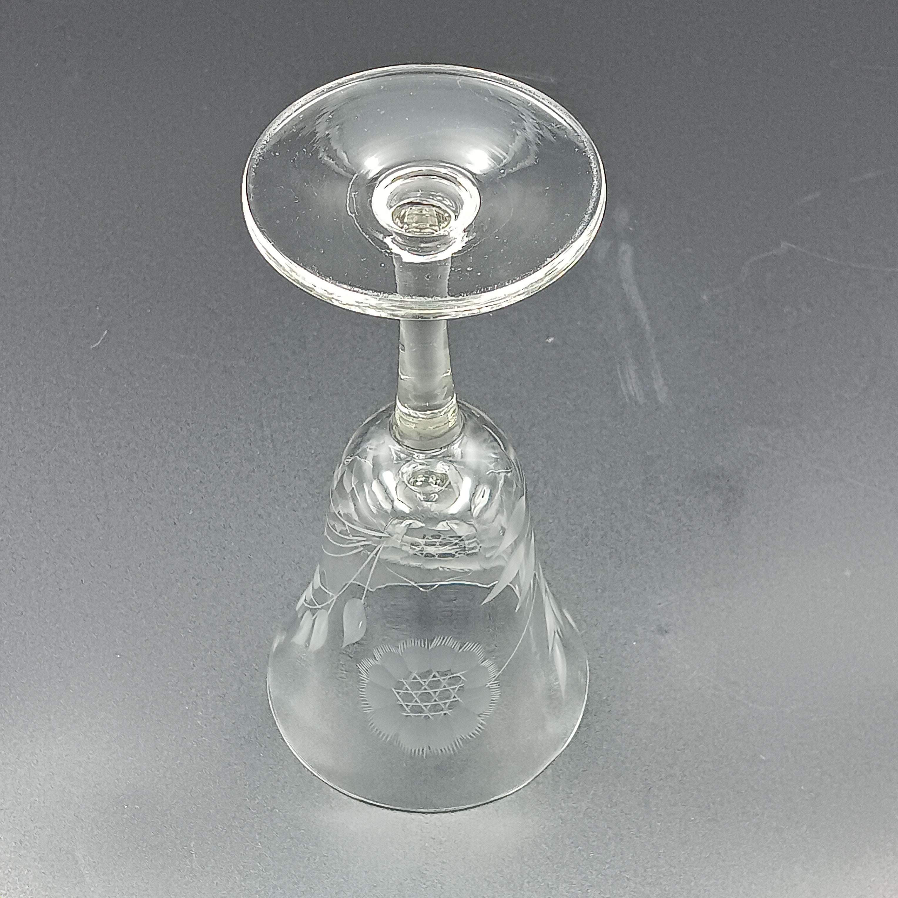 Vintage John Hughes cut crystal wine glass, featuring the iconic Corn Flower pattern, shown lying on its side against a dark reflective surface. The flared bowl displays intricate floral etching, with a slender stem and flat circular base