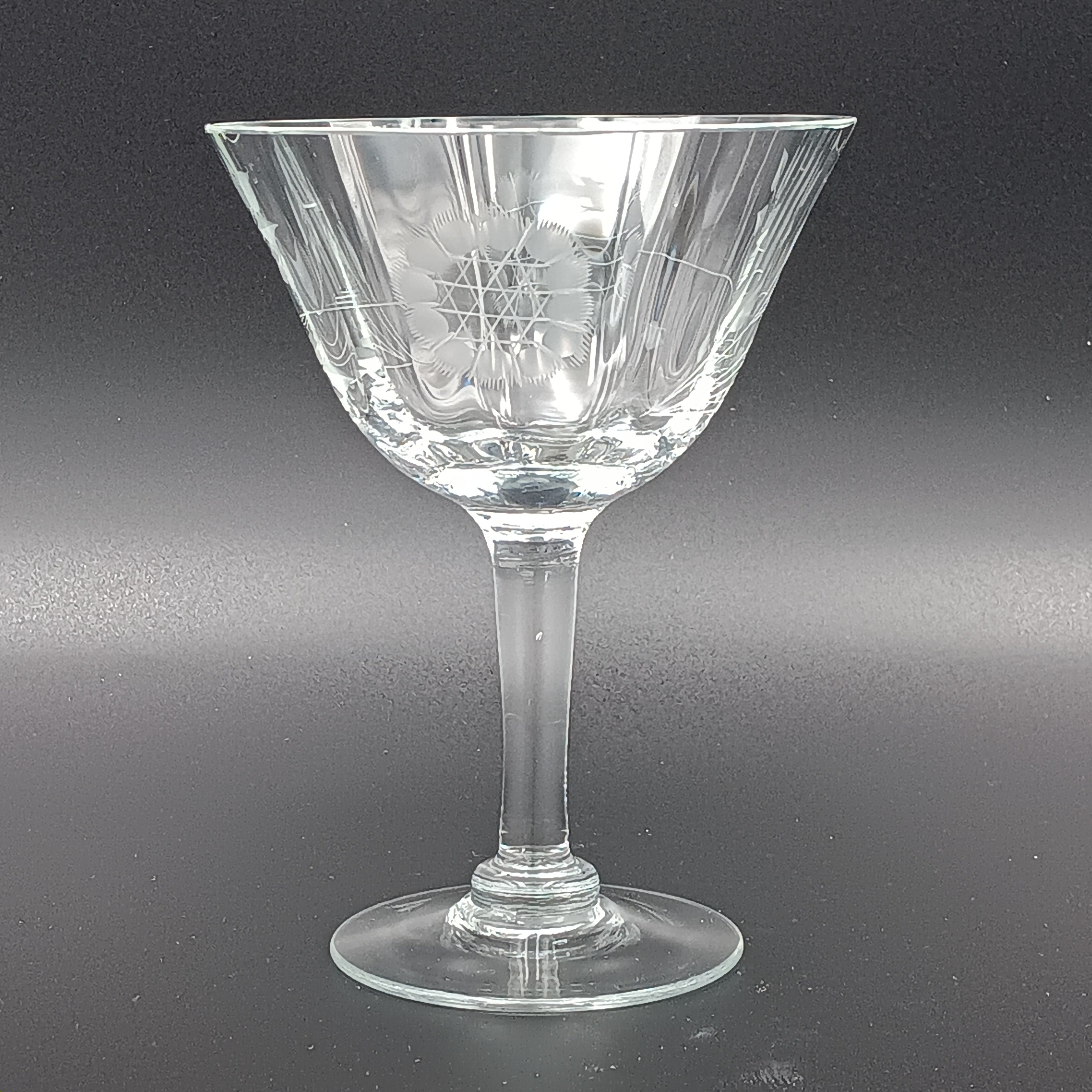 Vintage W J Hughes Cornflower champagne glass with etched floral and geometric patterns, lying horizontally on a dark surface with light highlighting its clear crystal design