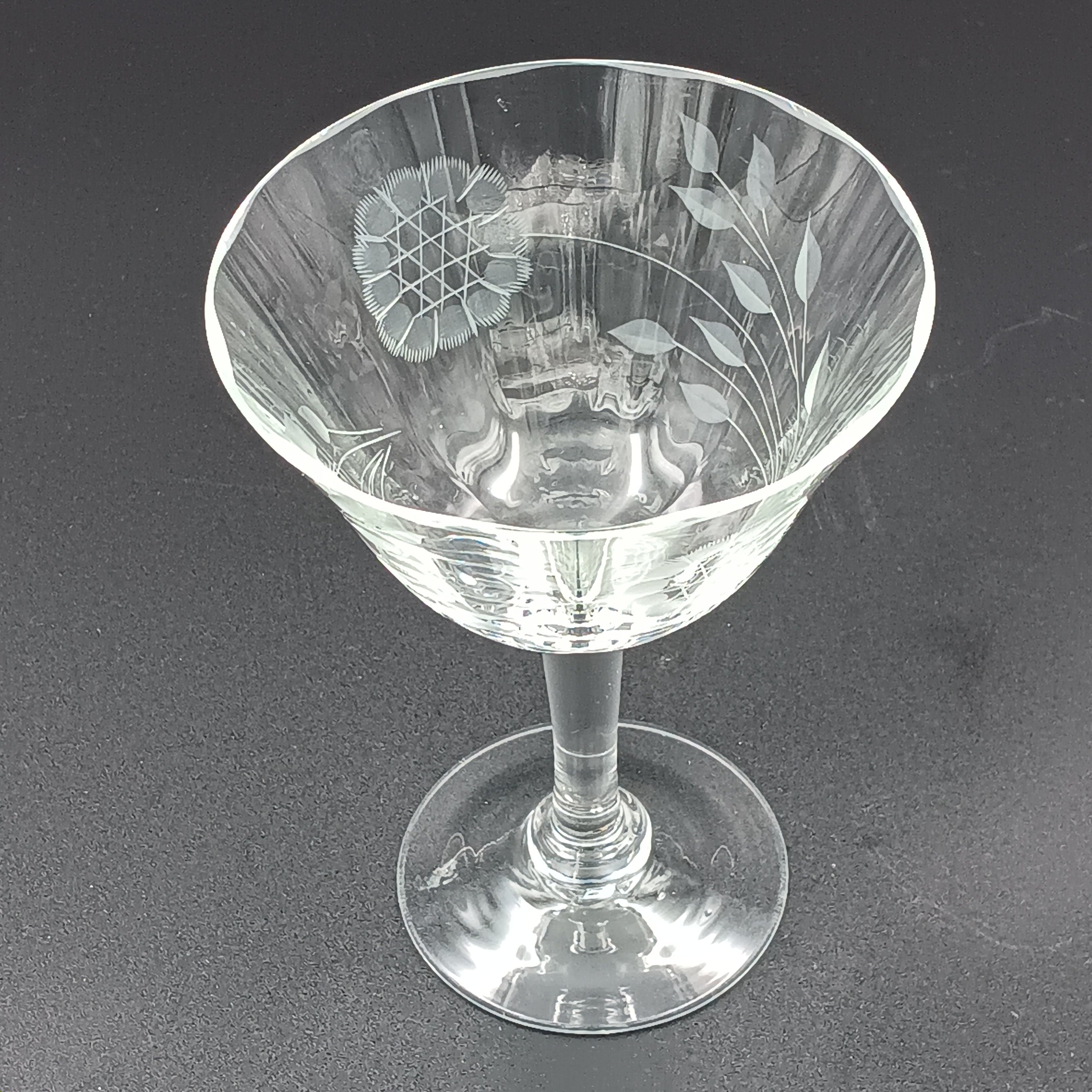 Vintage W J Hughes Cornflower champagne glass with etched floral and geometric patterns, lying horizontally on a dark surface with light highlighting its clear crystal design