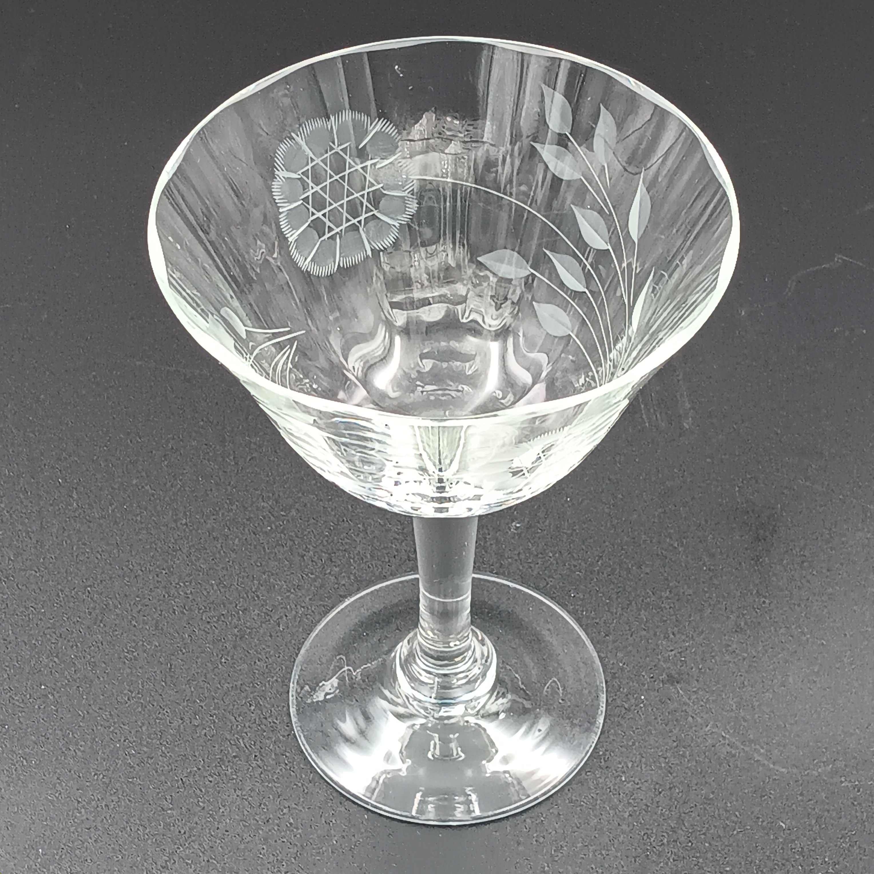 Vintage W J Hughes Cornflower champagne glass with etched floral and geometric patterns, lying horizontally on a dark surface with light highlighting its clear crystal design