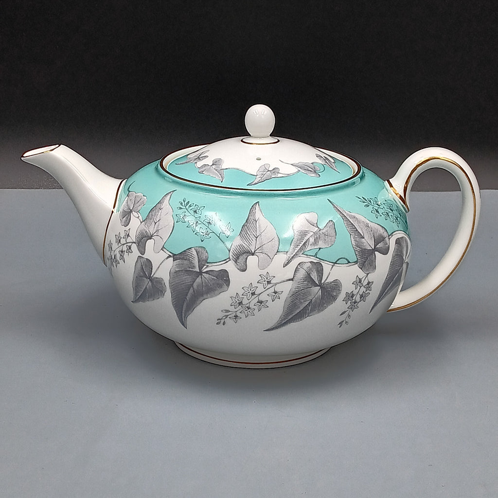 Wedgwood, Buxton, white porcelain teapot with a turquoise floral band, gold-accented handle and spout, and matching lid, displayed against a two-tone background.