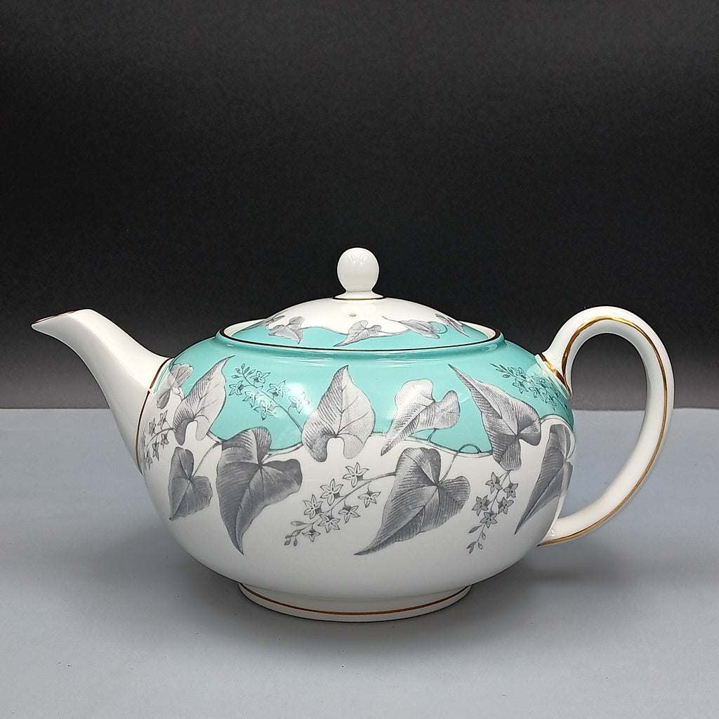 Wedgwood, Buxton, white porcelain teapot with a turquoise floral band, gold-accented handle and spout, and matching lid, displayed against a two-tone background.