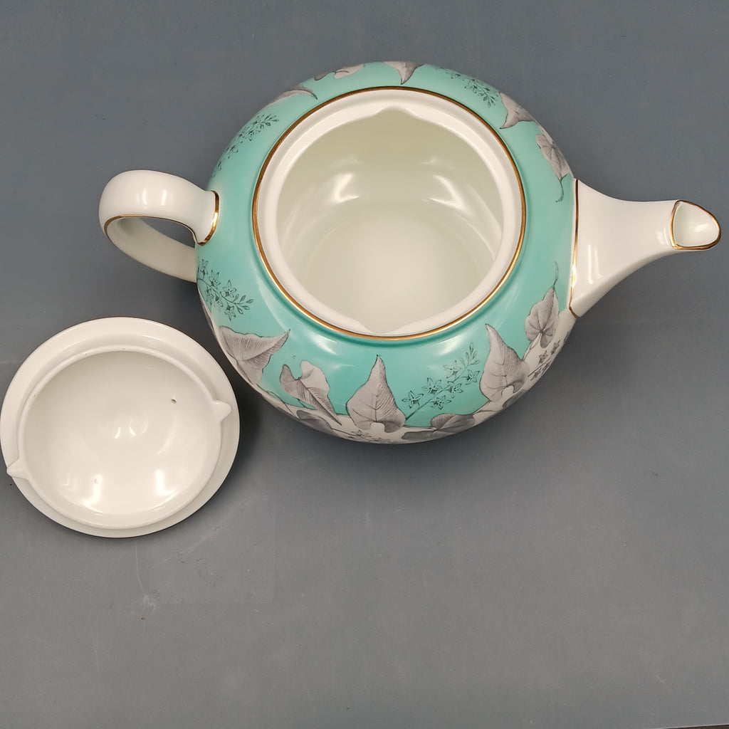 Wedgwood, Buxton, white porcelain teapot with a turquoise floral band, gold-accented handle and spout, and matching lid, displayed against a two-tone background.
