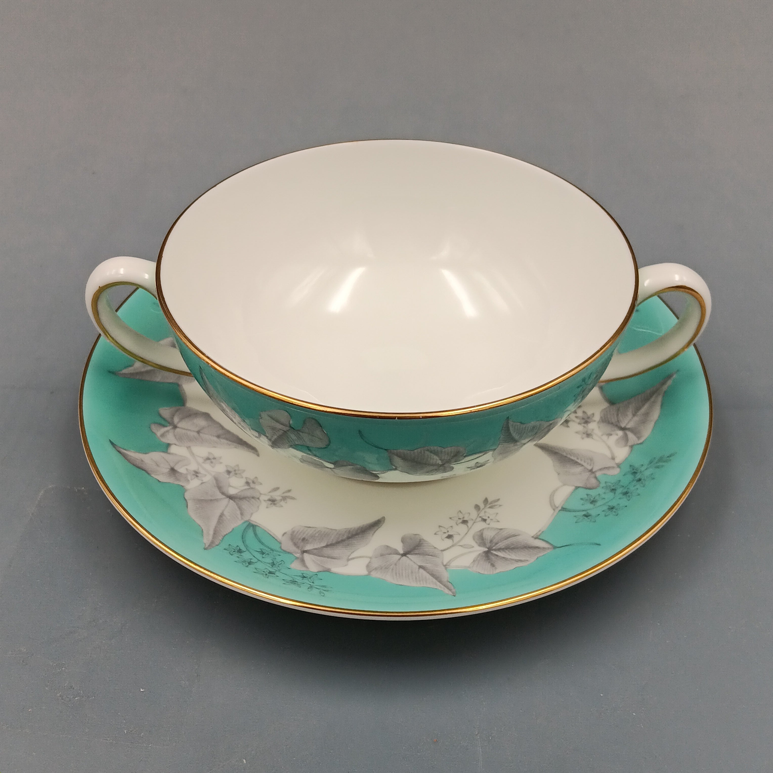 Wedgwood 'Buxton' double-handled soup bowl and saucer set featuring a turquoise background with gray and white floral design, accented by gold trim on edges; elegant English porcelain tableware ideal for collectors.