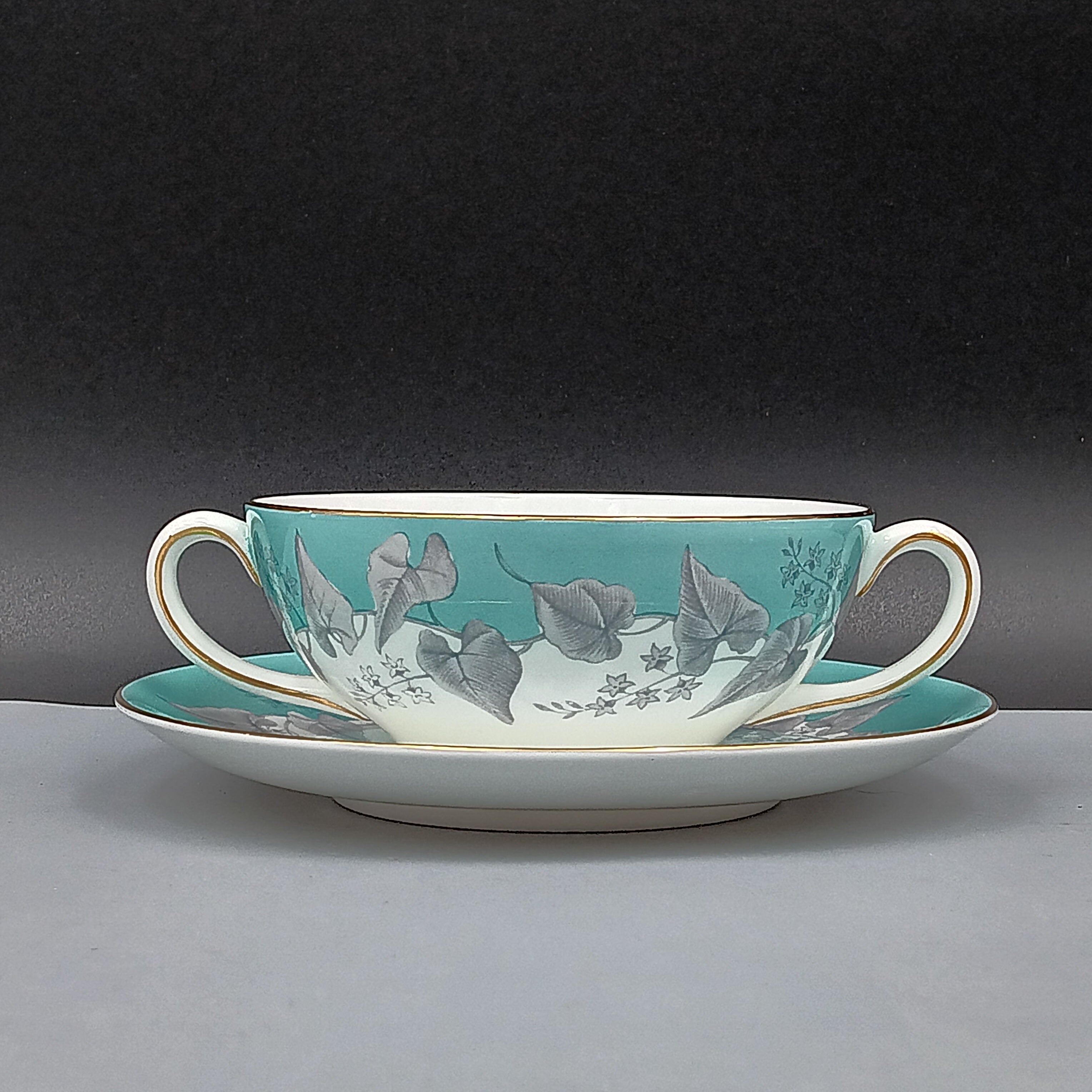 Wedgwood 'Buxton' double-handled soup bowl and saucer set featuring a turquoise background with gray and white floral design, accented by gold trim on edges; elegant English porcelain tableware ideal for collectors.